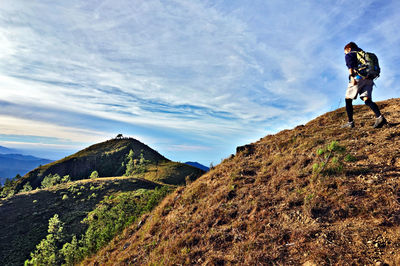 Low angle view of female hiker climbing mountain against sky during sunny day