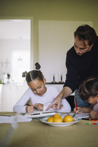 Father assisting to daughters while doing homework sitting at dining table