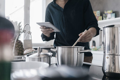 Man standing in kitchen reading news on his digital tablet while cooking