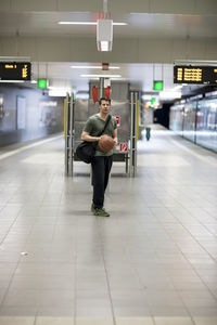 Portrait of young man with basketball walking at railroad station platform