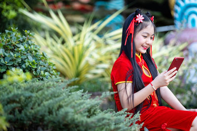 Cute girl using smart phone while sitting against plants