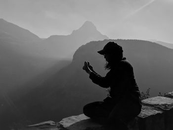 Side view woman sitting on retaining wall against sky