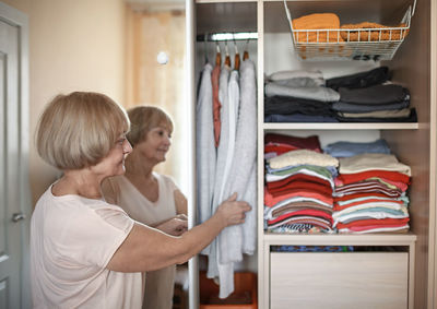 Senior woman holding clothing at cupboard