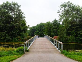 Footbridge amidst trees against sky