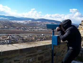 Man looking landscape through coin-operated binoculars against sky