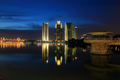 Illuminated buildings by river against sky at night