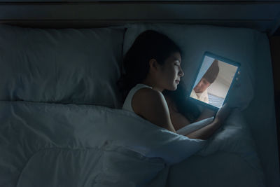 Young woman using mobile phone while lying on bed at home