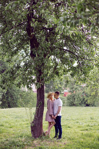 Man and a woman in love in a dress and hat are stand on a green field under a tree in summer