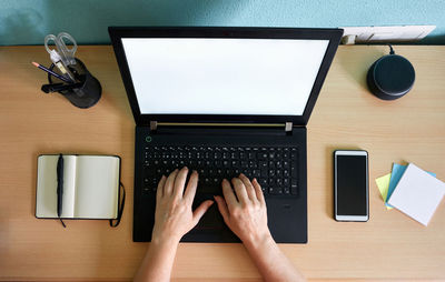 Unrecognizable woman writes on her laptop at a desk in her home