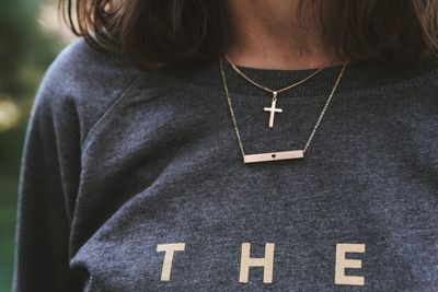 Midsection of teenage girl wearing crucifix necklace with text on t-shirt