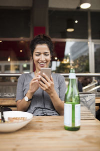 Smiling woman using mobile phone at wooden table in sidewalk cafe
