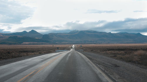 Empty road leading towards mountains against sky