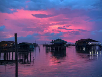 Wooden posts in sea against sky at sunset