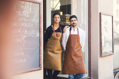 Portrait of confident male and female owners standing at grocery store entrance