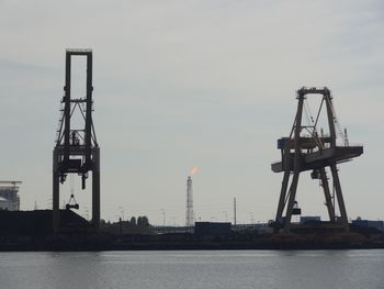 Crane at dock by sea against sky