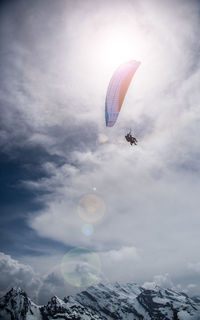 Low angle view of people paragliding against sky on sunny day