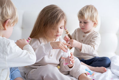 Cute boy tying sisters hair on bed at home