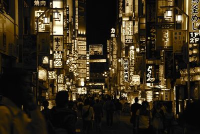 Group of people on illuminated street amidst buildings in city at night