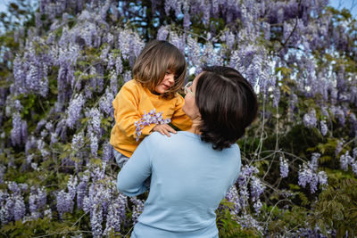 Rear view of woman standing against trees holding daughter in yellow clithes