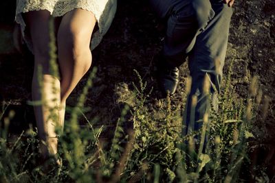 Low section of bride and groom leaning against wall on field