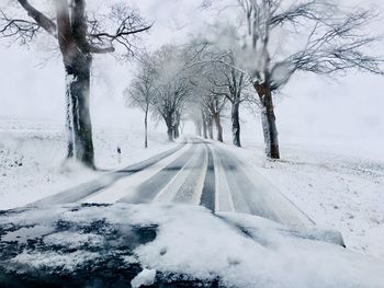 Snow covered road amidst trees during winter