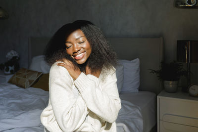 Happy woman wearing sweater hugging herself in bedroom