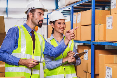 Man pointing at boxes while showing to female coworker in factory