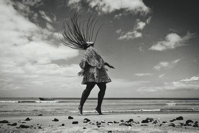 Rear view of woman walking on beach against sky