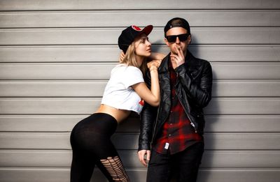 Portrait of handsome man smoking cigarette while beautiful woman looking at him against wall