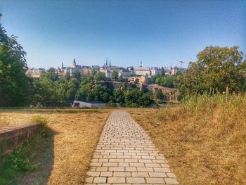 View of footpath in city against clear blue sky