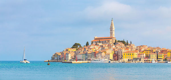 Sailboats in sea by buildings against sky