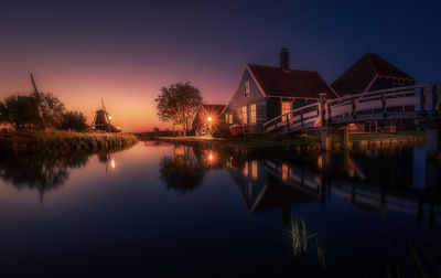 Illuminated buildings by lake against sky at night