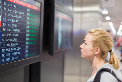 Side view of woman at arrival departure board at airport