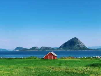 Nordic landscape along seashore, lawn, red old house facing a fjord islands, blue sky, summertime