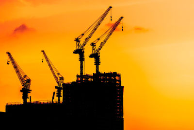 Low angle view of silhouette cranes at construction site against sky during sunset