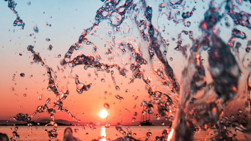 Close-up of water splashing against sky during sunset