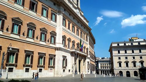 People on street against buildings in city during sunny day