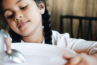 Close-up of girl looking down with spoon and plate at home
