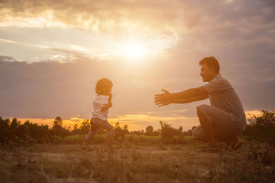 Father with daughter on field against sky during sunset