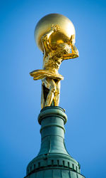 Low angle view of golden atlas sculpture against clear blue sky