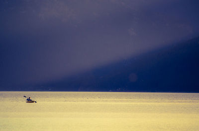 Distant view of person kayaking on sea against sky