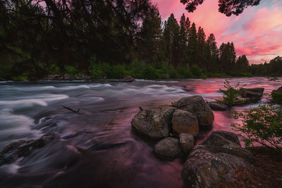 Rocks by river against sky at sunset