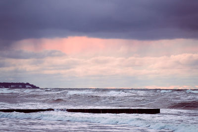 Scenic view of purple cloudy sky and sea with foaming waves. vintage long wooden breakwaters