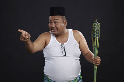 Smiling man gesturing while holding oil lamp against black background