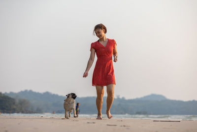 Full length of young woman playing with dog on beach
