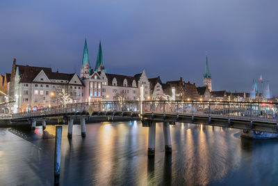 Illuminated bridge over river in city against sky at night