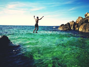 Man diving into sea against sky at beach