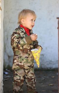 Cute boy wearing camouflage clothing looking away while holding popcorn