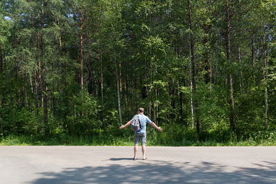 Full length of man standing on road amidst trees in forest