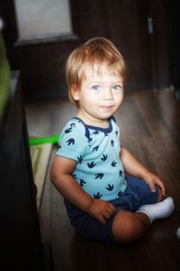 Cute boy looking away while sitting on floor at home